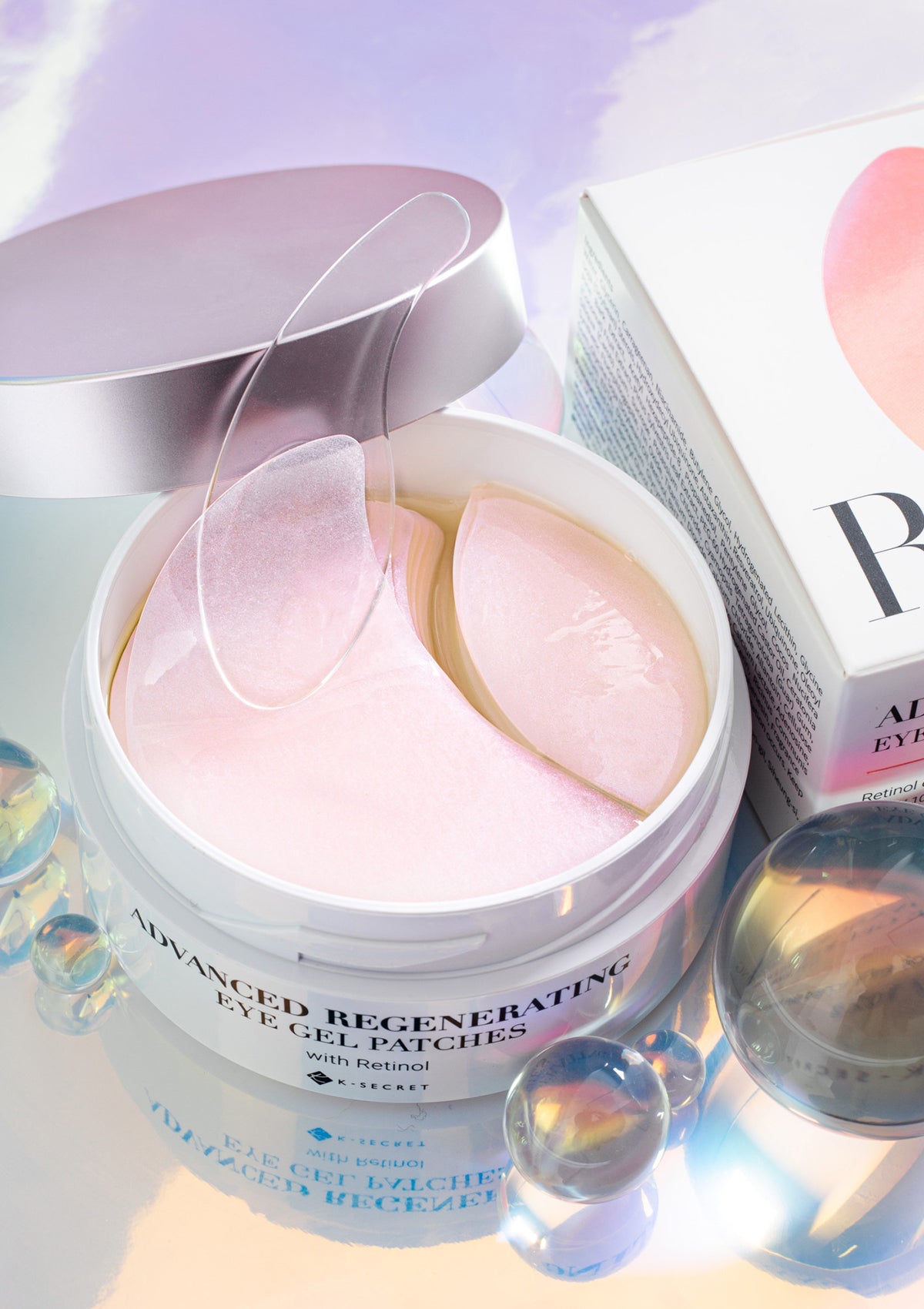 A box of K-SECRET Advanced Regenerating Eye Gel Patches with Retinol. The packaging is predominantly pink and white, with text and branding.